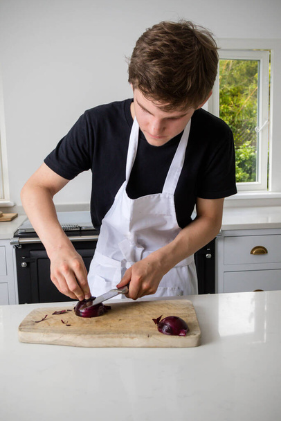 A teenage boy in a domestic kitchen chopping an oinion - Foto, afbeelding