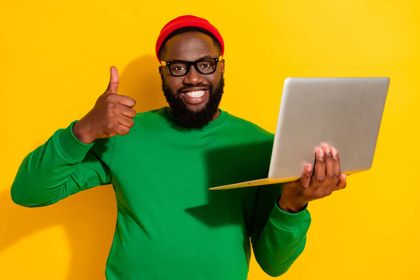 Portrait of attractive trendy successful cheerful guy using laptop showing thumbup isolated over bright yellow color background - Valokuva, kuva