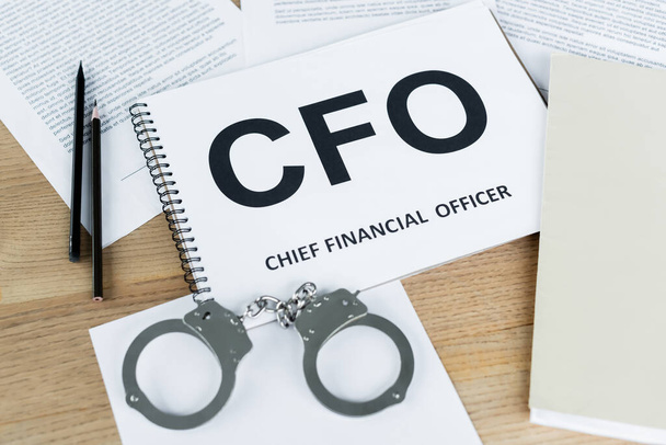 high angle view of notebook with cfo lettering near handcuffs and documents on desk - 写真・画像