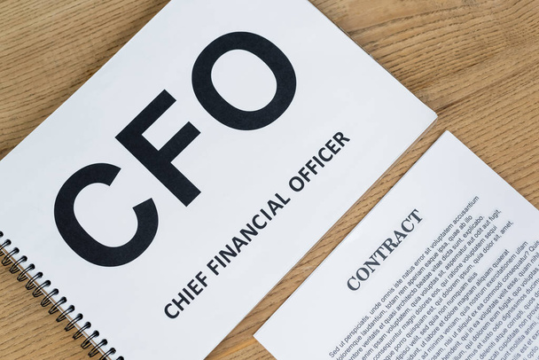top view of notebook with cfo abbreviation and chief financial officer lettering near contract on desk - Foto, afbeelding