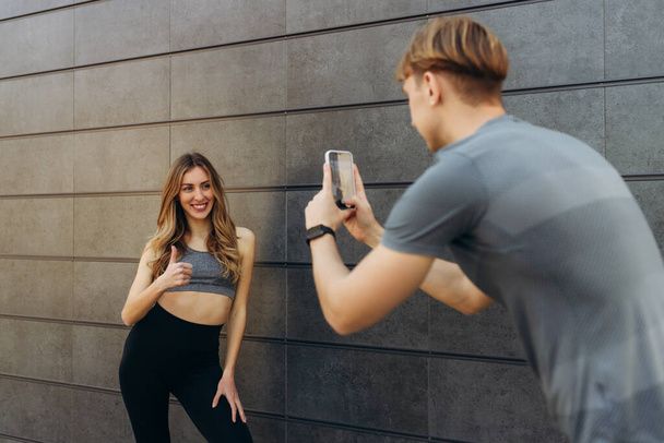 Imagen de un hombre guapo deportivo tomando fotos de su novia al aire libre en la pared. Deporte - Foto, imagen