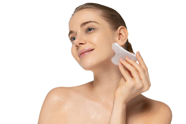 Retrato de tierna mujer joven haciendo masaje facial con herramienta cosmética especial aislado sobre fondo de estudio blanco - Foto, imagen