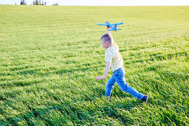 Chłopak lata z samolotem zabawki w lecie przez pole. Happy dziecko działa i bawi się z samolotem zabawki na zewnątrz. - Zdjęcie, obraz
