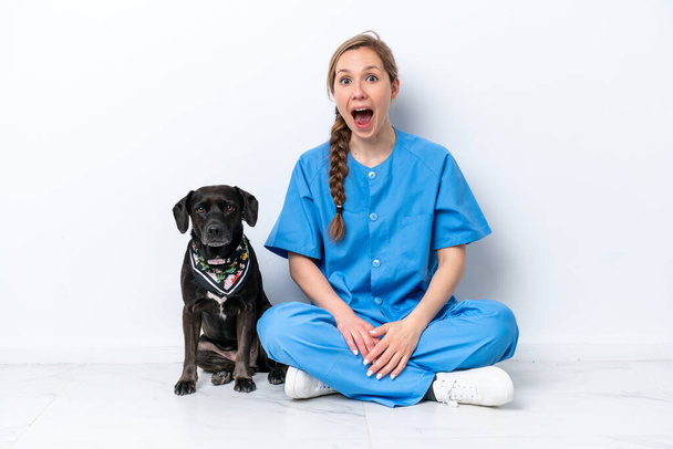 Young veterinarian woman with dog sitting on the floor isolated on white background with surprise and shocked facial expression - Φωτογραφία, εικόνα