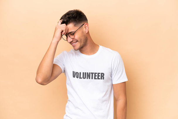 Joven voluntario caucásico aislado sobre fondo beige riendo - Foto, Imagen