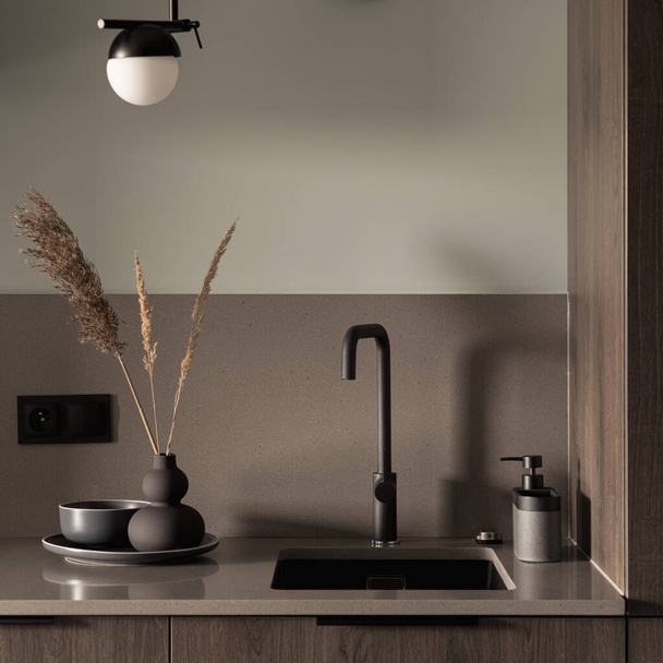 Close-up on stylish decorated kitchen countertop with black sink and tap, modern lamp and fancy vase, plate and bowl - Foto, Imagen