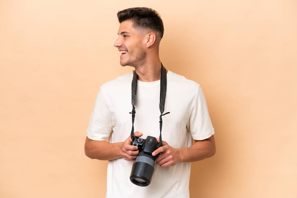 Jeune photographe homme caucasien isolé sur fond beige regardant côté - Photo, image