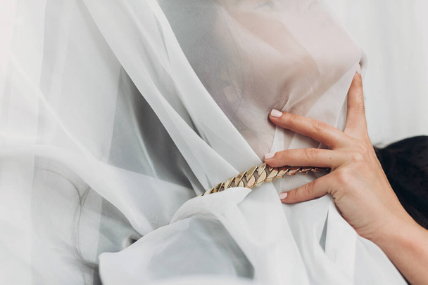 Portrait of young female covered with light fabric and hand on neck. Self care concept. Social isolation and pressure. Sensual woman under veil posing with golden necklace in room. Suffocate - Foto, Bild