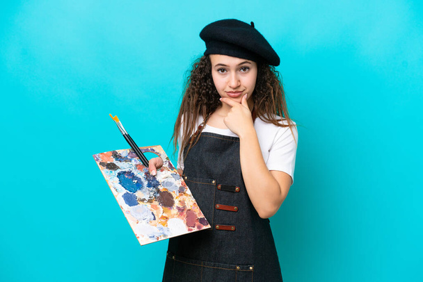 Young artist Arab woman holding a palette isolated on blue background thinking - Fotografie, Obrázek
