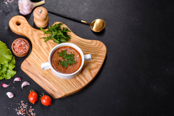 Sopa de tomate deliciosa fresca com especiarias e salsa em uma tigela branca em uma tábua de madeira contra um fundo de concreto escuro - Foto, Imagem