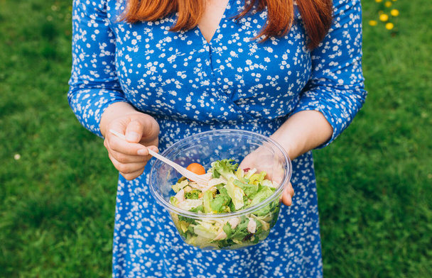 Mano de mujer sosteniendo un tazón con ensalada sobre un fondo natural aislado. Picnic saludable, pancarta de comida - Foto, Imagen