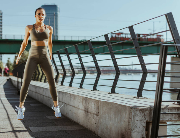 Pretty young woman in sportswear exercising on a river promenade - Photo, Image