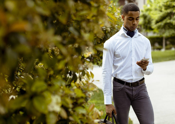 Schöner junger afroamerikanischer Geschäftsmann, der ein Mobiltelefon benutzt, während er auf einer Straße läuft - Foto, Bild