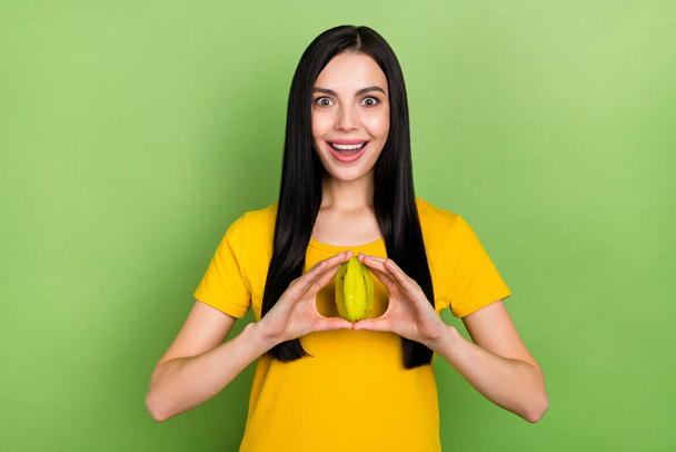 甘い印象の女性の写真は、熱帯フルーツを保持黄色のTシャツを着て隔離された緑の背景. - 写真・画像
