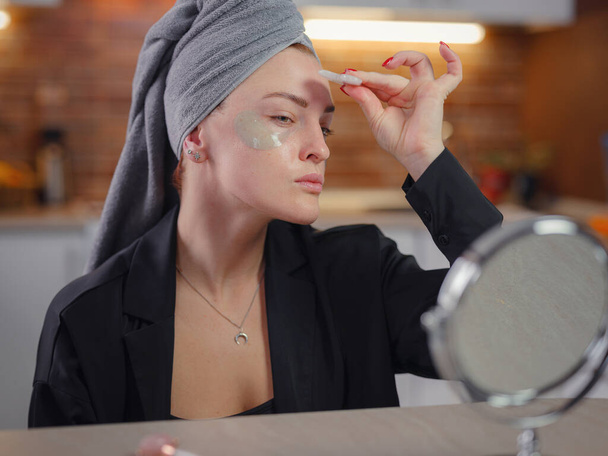jonge vrouw kijkt in de spiegel met behulp van facial gua sha jade board thuis. Liften, huidverzorging en lymfedrainage van het huidconcept. Beeldhouwen, tillen en anti-aging zorg. Huidverzorging en schoonheid thuis. - Foto, afbeelding