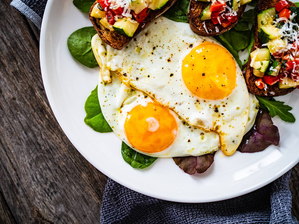 Sunny side up eggs, bruschetta and fresh vegetables on wooden table - Foto, afbeelding