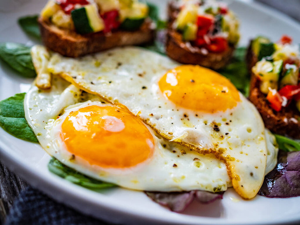 Sunny side up eggs, bruschetta and fresh vegetables on wooden table - Фото, изображение