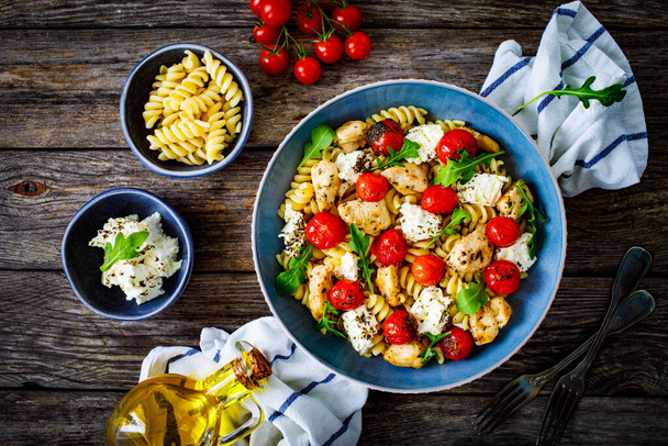 Roasted chicken nuggets, cherry tomatoes, feta cheese and fusilli served on wooden table - Foto, imagen