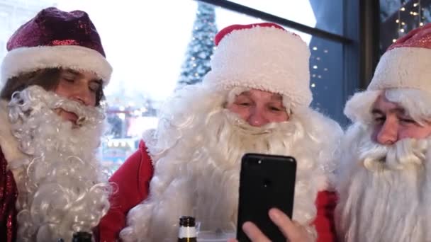 Three Santa Clauses use a smartphone to communicate with obedient children on Christmas Eve. Santa Claus is getting ready to deliver presents. Christmas magic concept - Footage, Video