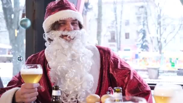 Babbo Natale con una grande barba grigia sta bevendo birra da un bicchiere, si sta rilassando con gli amici in un caffè. Spirito di Natale, preparazione per Capodanno - Filmati, video