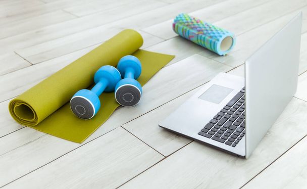 Laptop met halters, tapijt en massageroller op de vloer. Online fitness klas, of sport tutorial - Foto, afbeelding