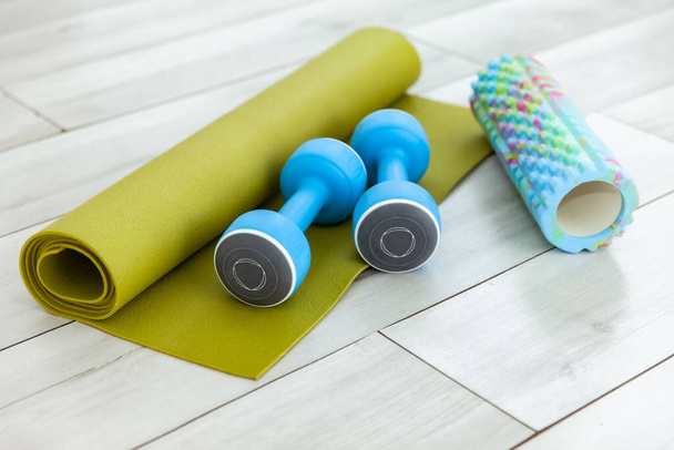 Dumbbells, rug and massage roller on the floor indoors. Healthy lifestyle concept - Photo, Image