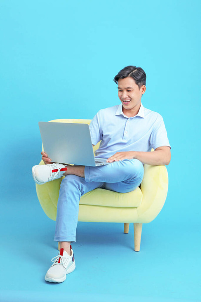 Asian handsome and cheerful young man working on laptop and sitting on sofa, isolated on background - Valokuva, kuva