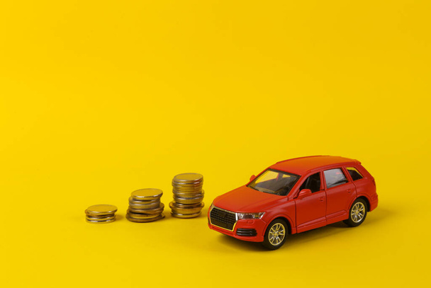 Παιχνίδι κόκκινο αυτοκίνητο μοντέλο με μια στοίβα κέρματα σε κίτρινο φόντο. Εξοικονόμηση χρημάτων, επένδυση, αγορά αυτοκινήτου έννοια - Φωτογραφία, εικόνα