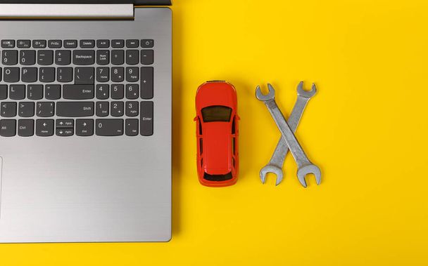 Laptop met speelgoedauto en sleutels op een gele achtergrond. Online diagnostiek, service center, auto reparatiewerkplaats. Bovenaanzicht - Foto, afbeelding