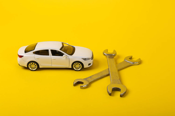Modelo de carro de brinquedo com uma chave em um fundo amarelo. Serviço de automóveis, conceito de reparação. - Foto, Imagem