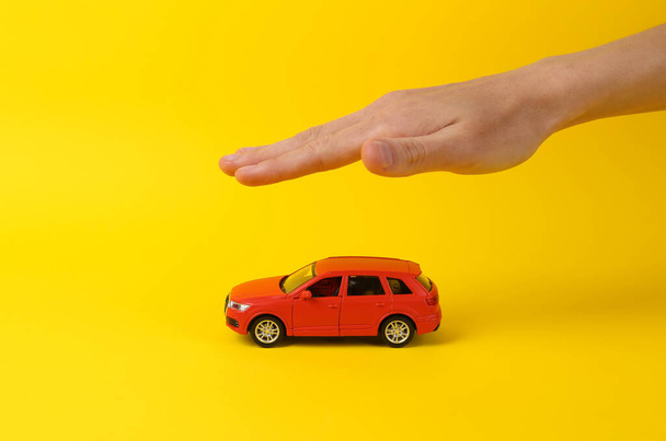 Concepto de autoprotección, seguro. Entregar modelo de coche de juguete sobre fondo amarillo - Foto, imagen
