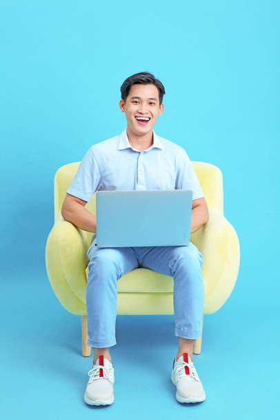 Work from home concept with an Asian young handsome guy, with laptop computer, isolated on blue background - Photo, Image