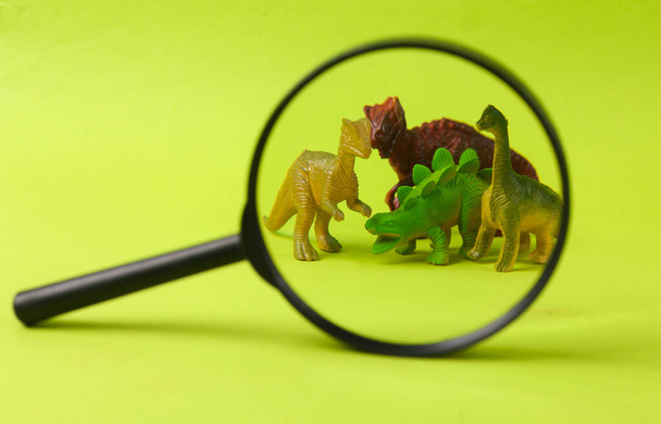 Oyuncak dinozorlar yeşil arka plandaki büyüteçle büyütüldü - Fotoğraf, Görsel