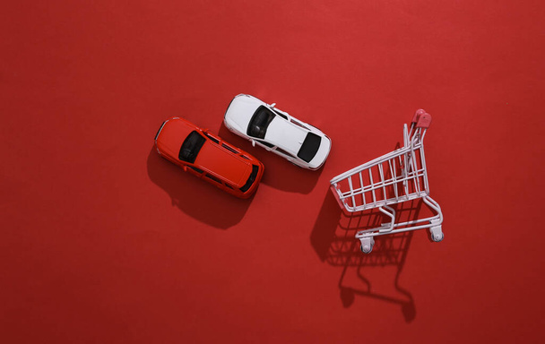 Araba konsepti alıyorum. Alışveriş arabası ve oyuncak arabalar kırmızı arka planda. - Fotoğraf, Görsel