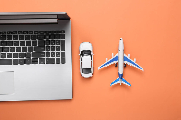 Концепция путешествий, бронирование онлайн. Ноутбук с автомобилем и самолетом на коралловом фоне - Фото, изображение