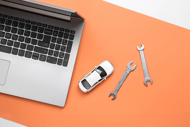 Online auto service. Laptop met speelgoedauto en sleutels op koraalondergrond. Bovenaanzicht - Foto, afbeelding
