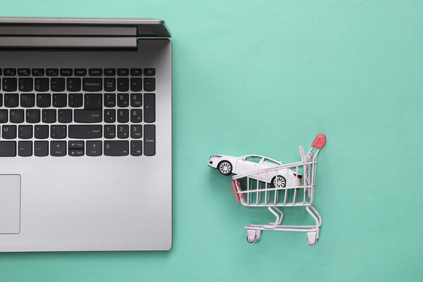Ordenador portátil con un coche de juguete en un carrito de compras sobre un fondo azul. Compra de coche en línea. Vista superior - Foto, imagen