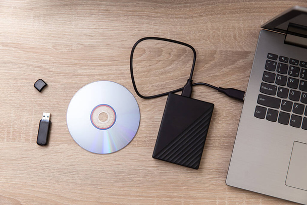 Ψηφιακοί θεματοφύλακες πληροφοριών. Εξωτερικός σκληρός δίσκος, cd και usb flash drive, laptop σε ξύλινο τραπέζι - Φωτογραφία, εικόνα