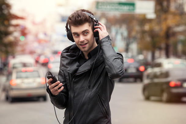 muž ve sluchátkách na ulici. Stojící s telefonem v ruce - Fotografie, Obrázek