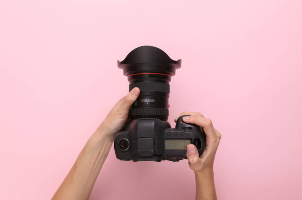 Женщины держат профессиональную цифровую камеру на розовом фоне. Вид сверху - Фото, изображение