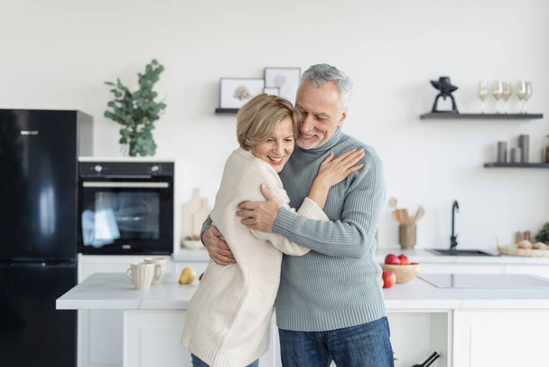 Concept of tenderness and romantic in relationships. Married and happy couple hugging and dancing in bright cozy kitchen together, enjoying the sensual moment. True love, sincere people - Photo, image