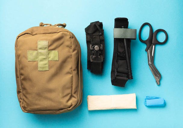 Military first aid kit with a medical tourniquet to stop the blood, gloves, tourniquets, gauze on a blue background. Place to copy. View from above. Flat lay. - Foto, Bild