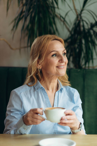 Bir fincan kahveyle orta yaşlı güzel bir kadının yakın plan portresi. - Fotoğraf, Görsel