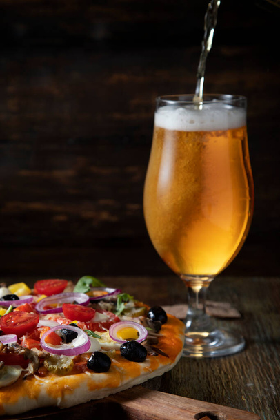 Σπιτική πίτσα vegan και μπύρα χύνεται σε ένα ποτήρι - Φωτογραφία, εικόνα