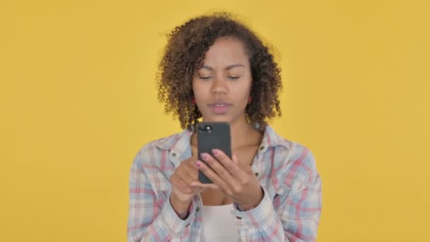 Afrykańska kobieta świętuje na smartfonie na żółtym tle  - Materiał filmowy, wideo