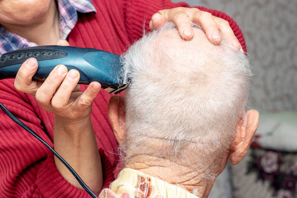 Woman haircut an elderly man with a trimmer. Haircut at home - Photo, image