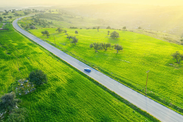 Landschaft grüne Landschaft mit einem Auto, das eine asphaltierte Straße hinunterfährt und einem Auto, Drohnenblick von oben - Foto, Bild
