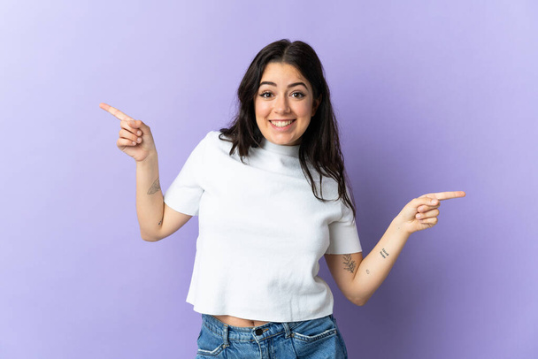 Young caucasian woman isolated on purple background pointing finger to the laterals and happy - Photo, image