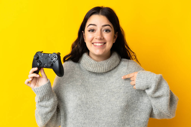 Sarı arkaplanda video oyunu kontrolörüyle oynayan kadın şaşırmış yüz ifadesi ile - Fotoğraf, Görsel