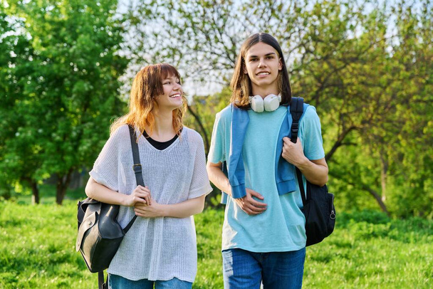 Portrait of teenage young guy and girl students outdoor. Couple of young people with backpacks, on green lawn of campus. Teenagers, lifestyle, joy, friendship, education concept - Foto, Imagen